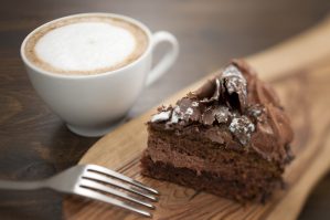 Slice of buttercream handmade Chocolate cake with a cappuccino. Shallow shifted focal plane with tilt and shift lens.
